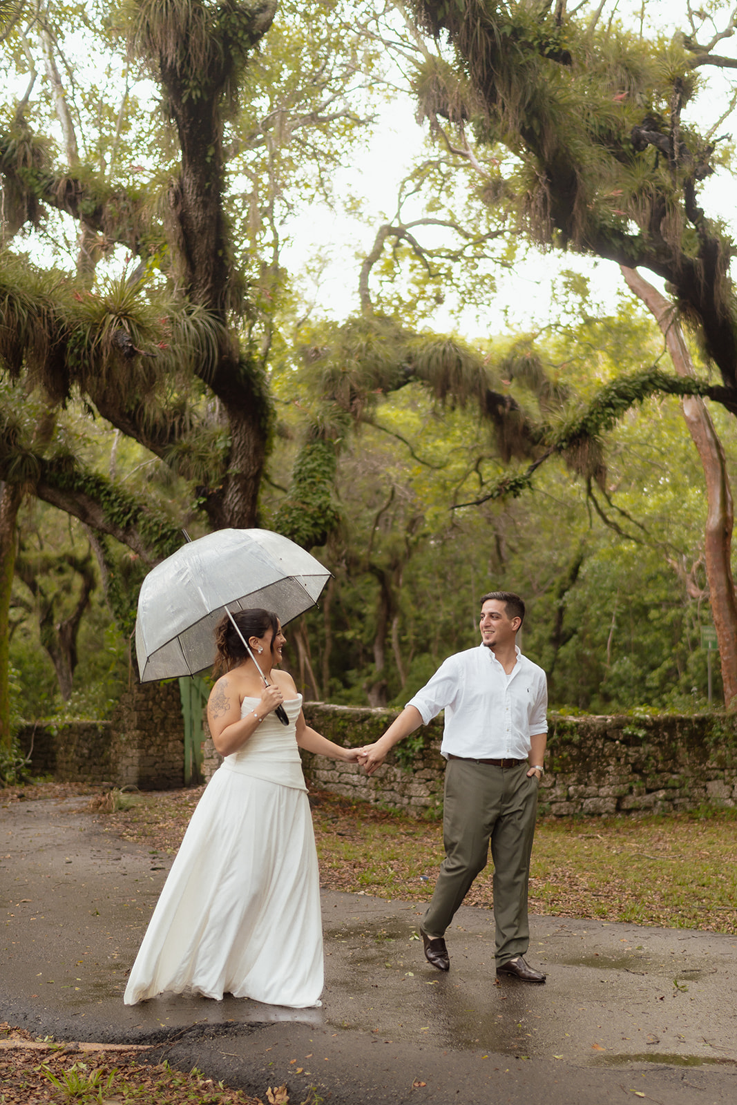 Man and woman hold hands with clear umbrella during engagement session